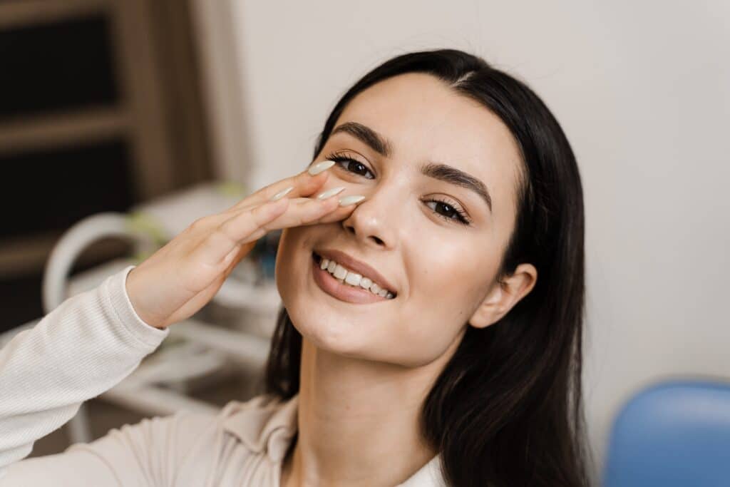 Woman smiling and touching her nose after rhinoplasty in Kansas City